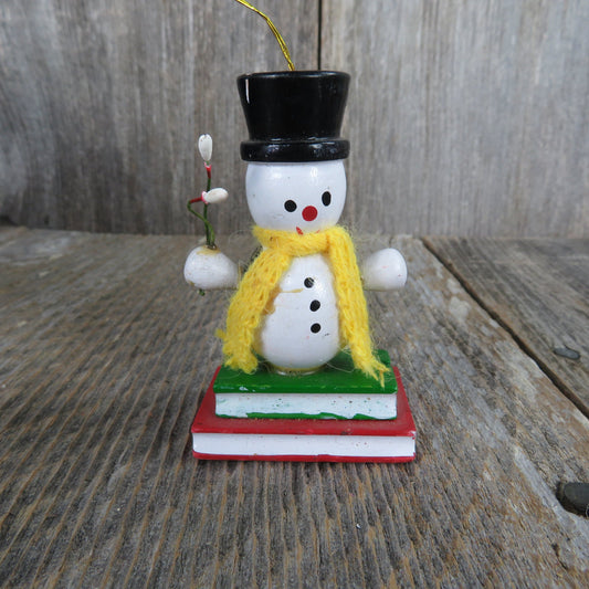 Vintage Snowman Holding Marshmallows Wood Ornament Yellow Scarf Black Hat and Vest Standing On Books Wood Christmas